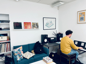 Someone playing a keyboard in the Link Learning office, with a green sofa and records on the wall