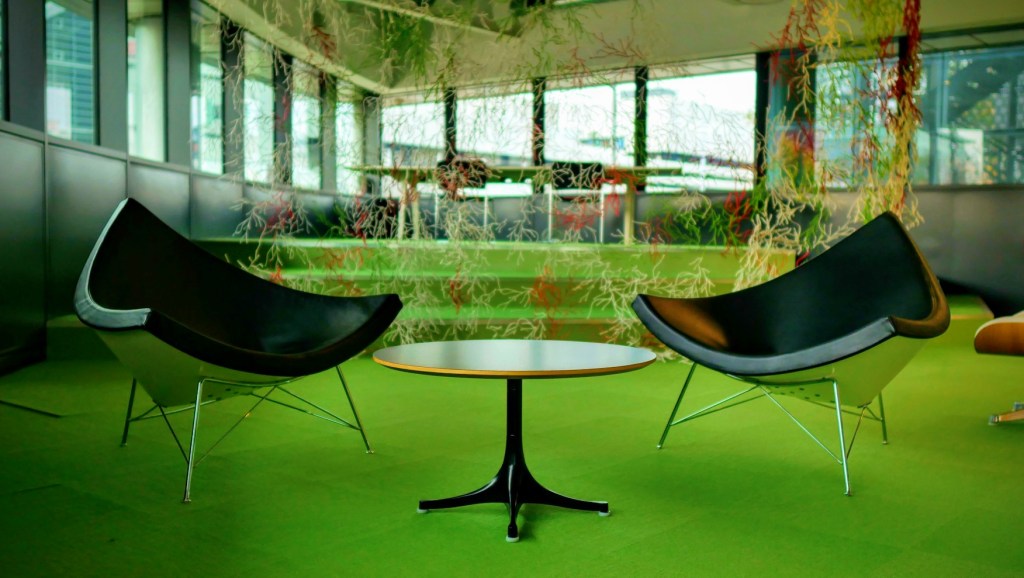 Two black lounge chairs and a small table under hanging plants at Electric Works