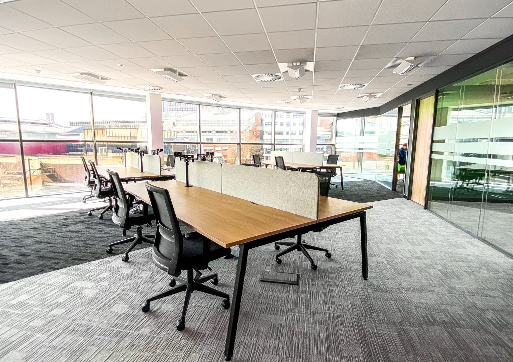 Open-plan office with rows of desks and floor-to-ceiling windows