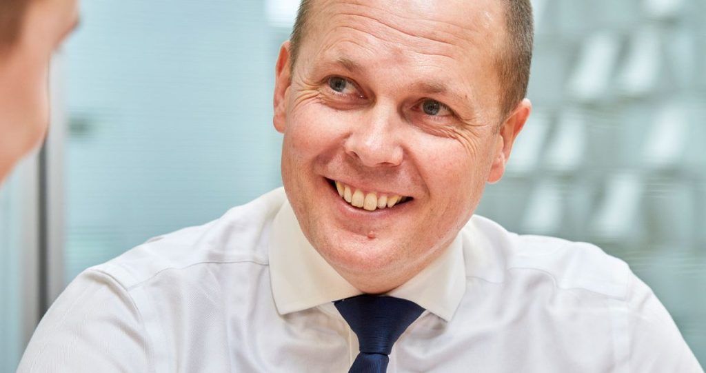 A smiling man in a white shirt and navy tie