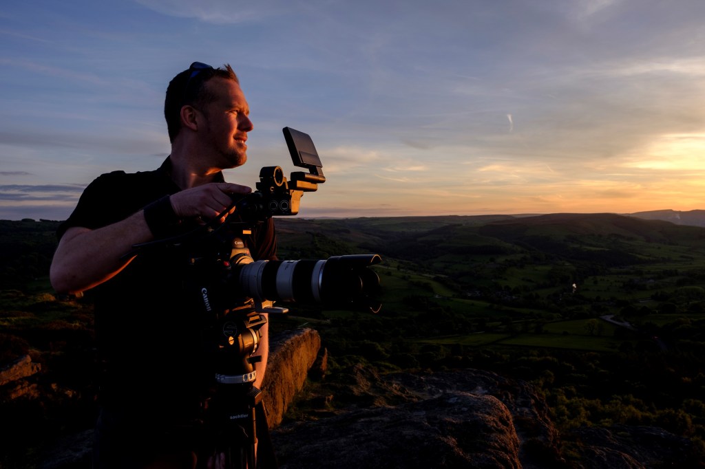 A filmmaker with a camera on a hilltop at sunset